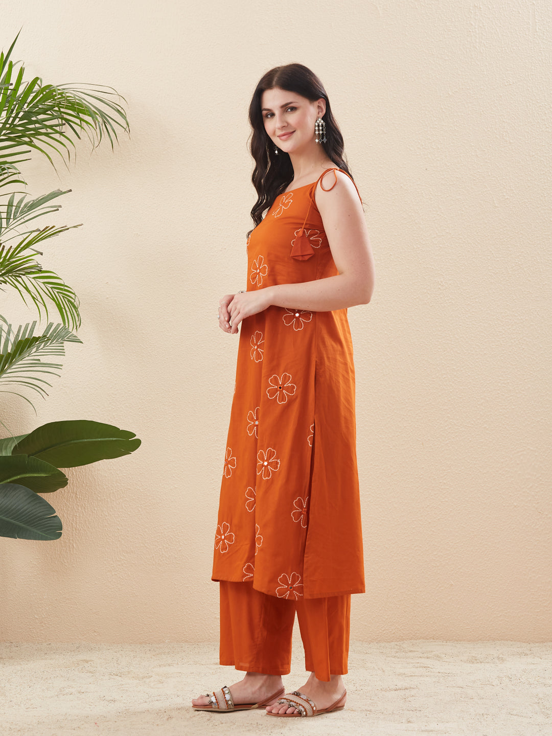 Woman wearing an orange embroidered outfit standing against a beige background with a plant on the left. Orange Cotton Embroidered Kurta with Palazzo Set for Women