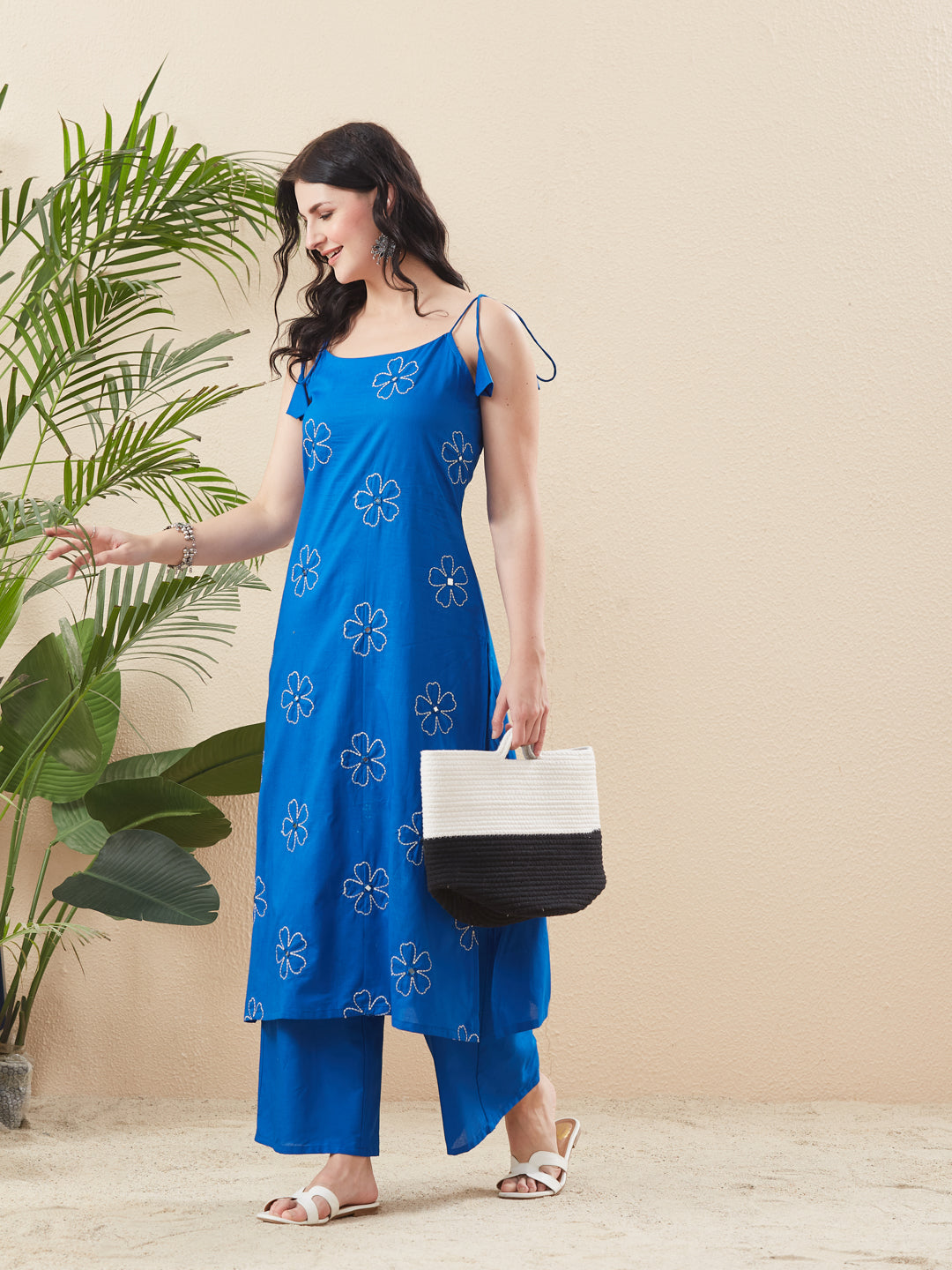 Woman in a blue floral dress holding a handbag next to a plant against a beige wall. Blue Cotton Embroidered Kurta with Palazzo Set for Women