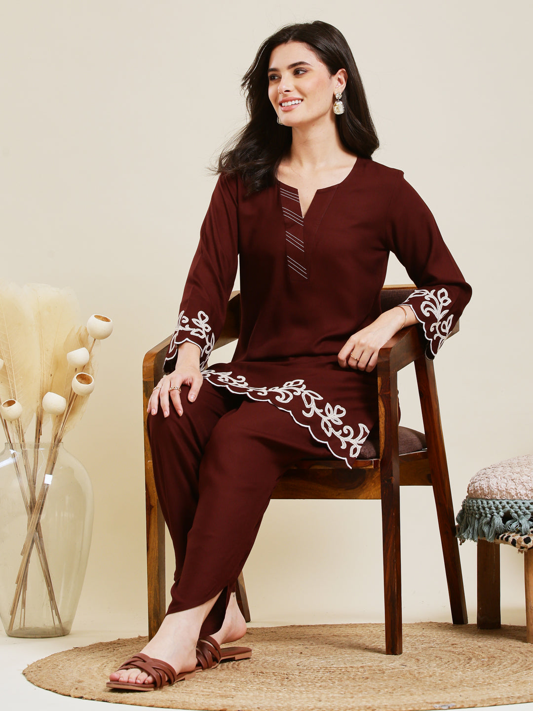 Woman sitting on a chair wearing a maroon traditional outfit with white embroidery. Coffee Rayon Embroidered Co-ord Set for Women