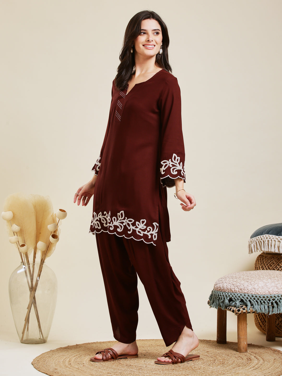 Woman wearing a maroon embroidered outfit standing in a room with decorative elements. Coffee Rayon Embroidered Co-ord Set for Women