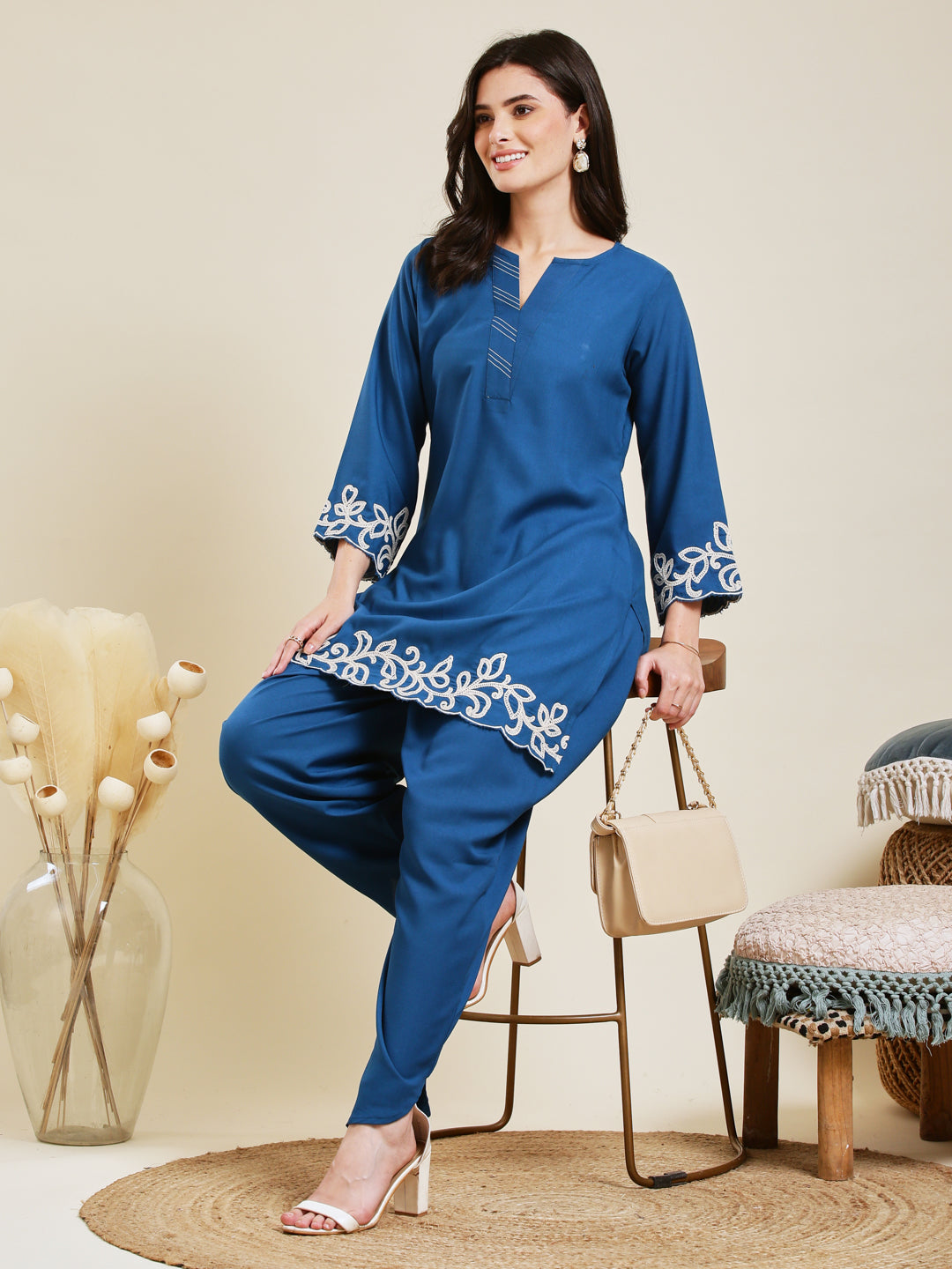 Woman wearing a blue outfit with white embroidery sitting on a chair. Teal Blue Rayon Embroidered Co-ord Set for Women