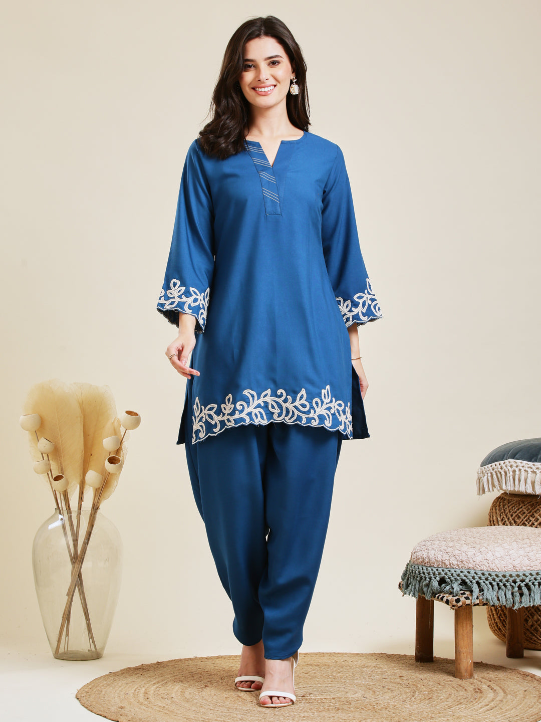 Woman wearing a blue embroidered outfit standing in a room with decorative elements. Teal Blue Rayon Embroidered Co-ord Set for Women