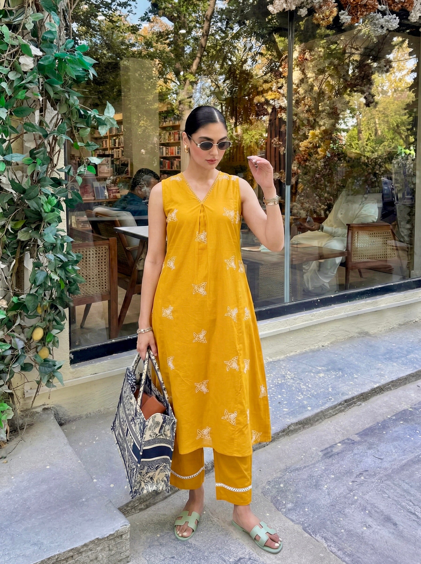 Woman in a yellow outfit standing outdoors near a building with greenery.
