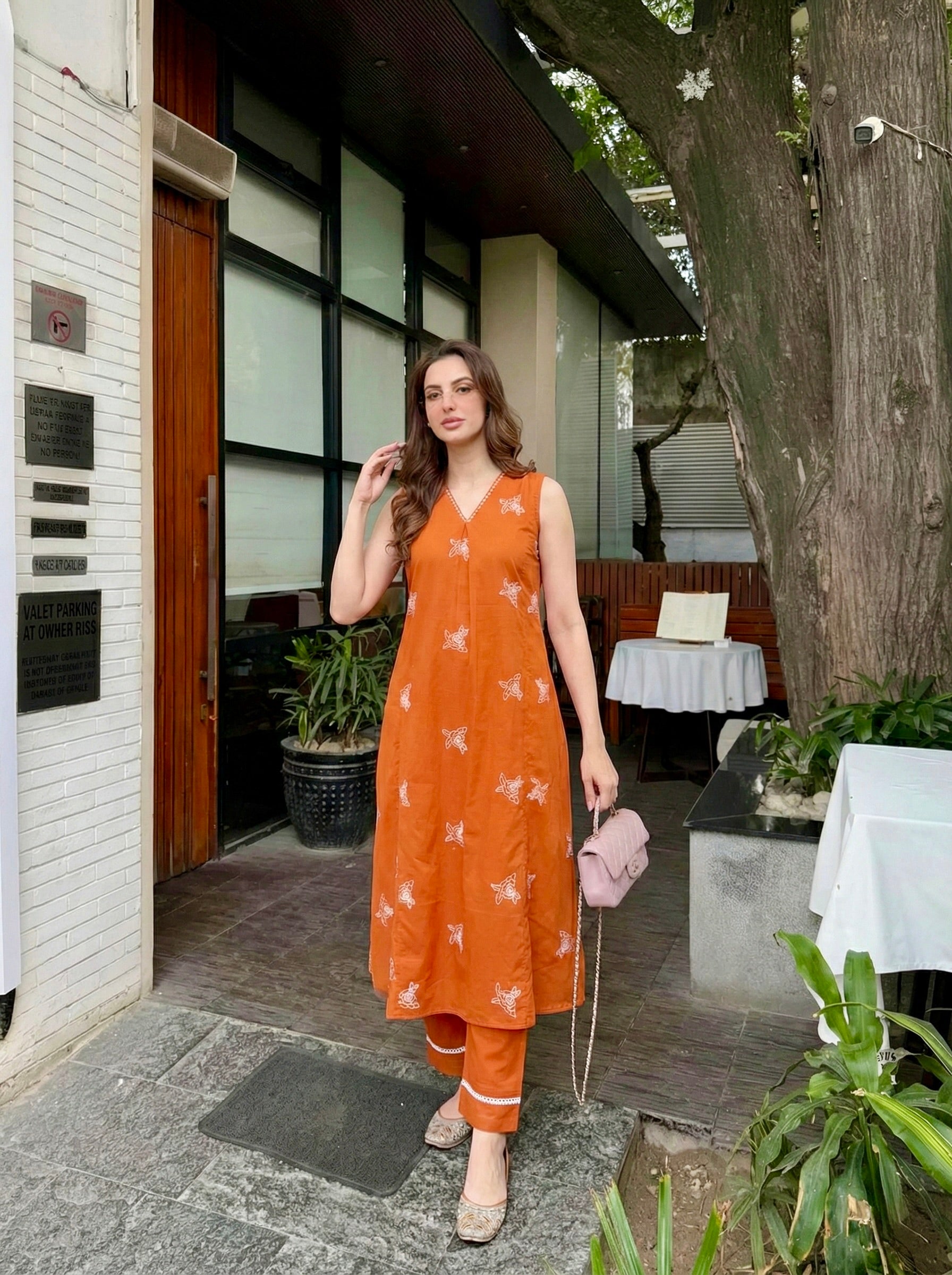 Woman in an orange dress standing outdoors near a building entrance.