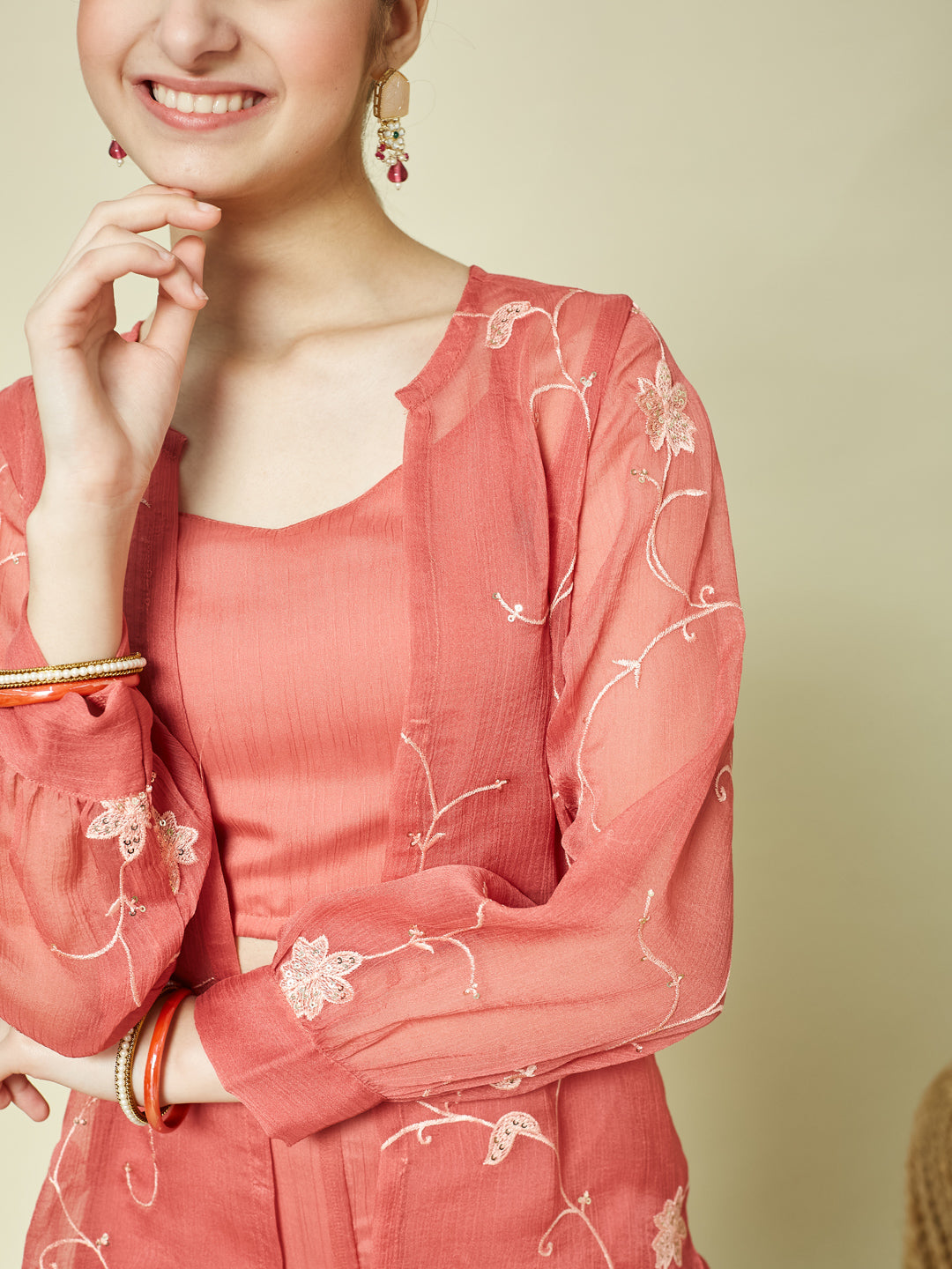 Woman wearing a coral pink traditional outfit with floral embroidery on a beige background Women Pink Crop Top with Palazzo and Shrug Set