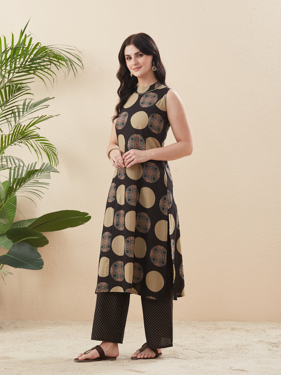 Woman wearing a black and gold patterned outfit standing next to a plant on a beige background Women’s Black Cotton Printed Straight Kurta Pant Set