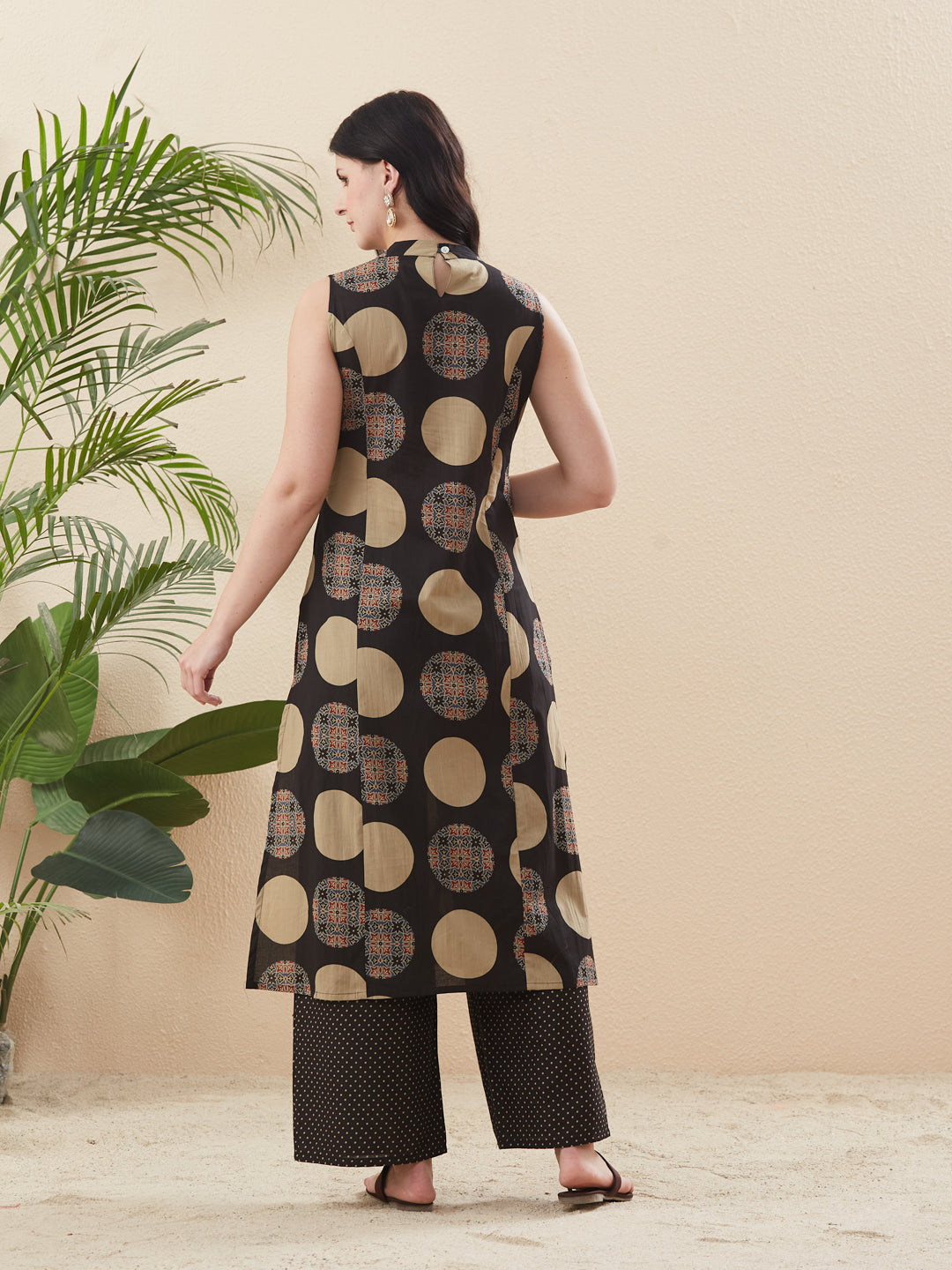 Woman wearing a patterned dress standing next to a plant against a beige wall. Women’s Black Cotton Printed Straight Kurta Pant Set