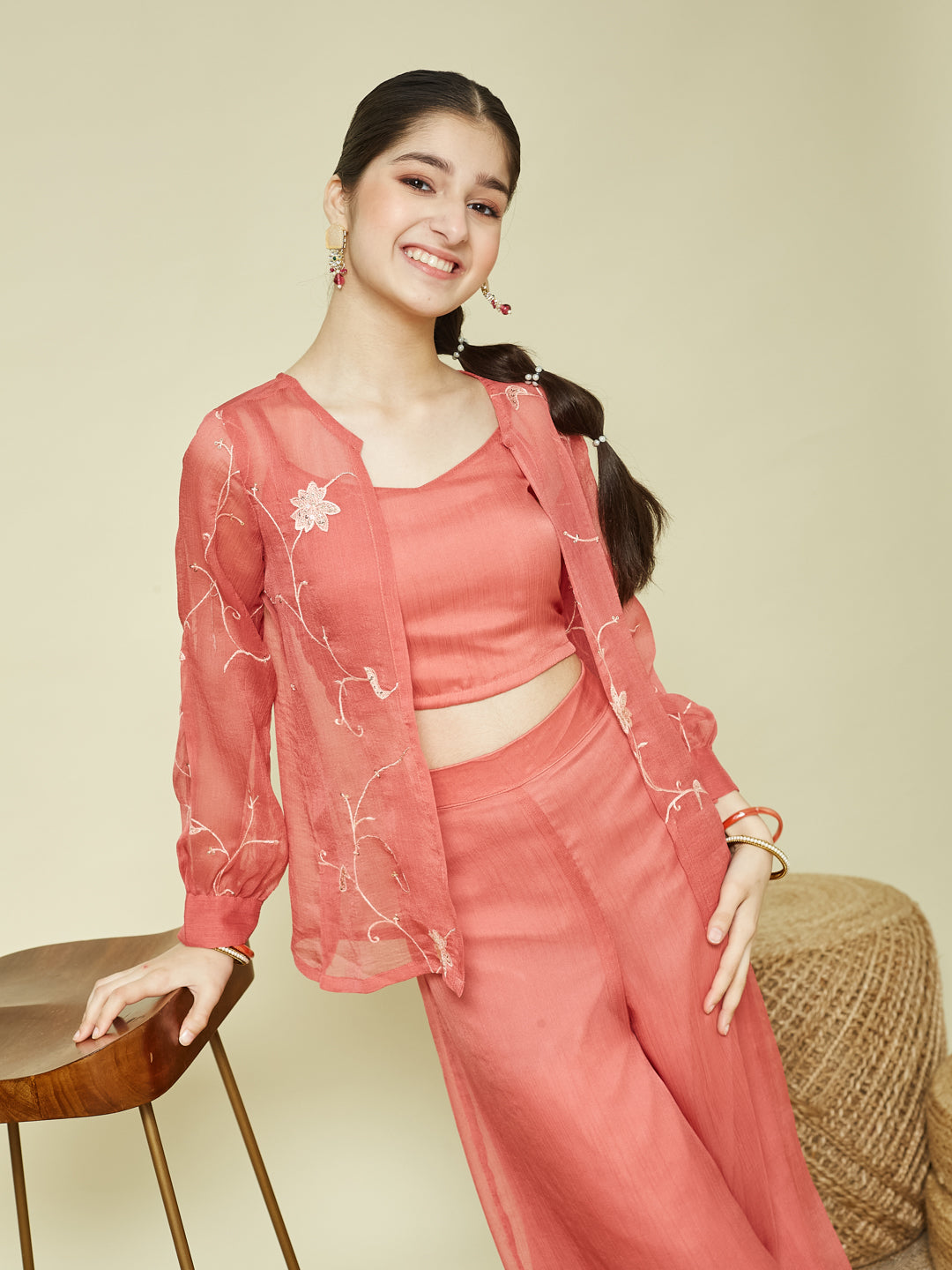 Woman in a pink outfit sitting on a chair with a beige background Women Pink Crop Top with Palazzo and Shrug Set
